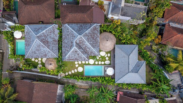 An aerial view of a residential area with multiple houses, a swimming pool, and a garden with a circular stone pattern. - Beta Villa by Betterplace (Ubud)