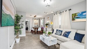 A modern living room with a white sofa, a coffee table, and a dining area with a table and chairs.