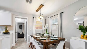 A dining area with a wooden table set for four, white chairs, a white cabinet, and a mirror on the wall.