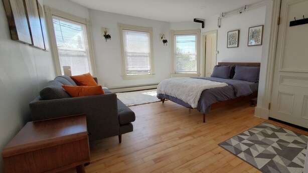 A bedroom with a bed, a sofa, a small table, and a window. - Stylish Studio in the Queen City
 (Burlington)