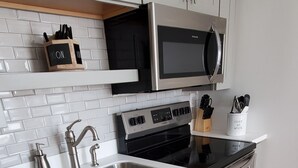 A modern kitchen with white cabinetry, stainless steel appliances, and a wooden floor. - Stylish Studio in the Queen City
 (Burlington)