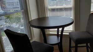 A room with a round table and two chairs, large windows with blinds, and a view of the outside. - Stylish Studio in the Queen City
 (Burlington)