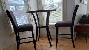 A room with a wooden floor, two black chairs, a small table, and a window with blinds. - Stylish Studio in the Queen City
 (Burlington)