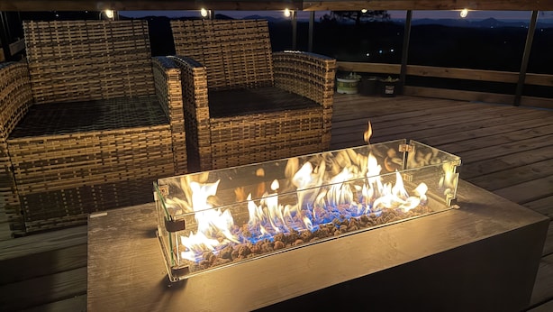 Una chimenea con recinto de vidrio, mobiliario de mimbre y vistas al exterior.
