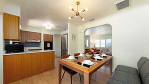 Cocina compacta con armarios de madera, una mesa de comedor lista para cuatro personas y un sofá gris en la sala.