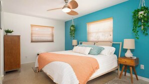 Un dormitorio con cama, dos mesitas de noche, ventilador de techo y dos ventanas con persianas.