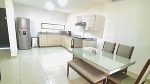A modern kitchen with a dining area, featuring a glass table and wooden chairs, a built-in microwave, and a stainless steel refrigerator. - Spacious Cancun Retreat • Pool • Sleeps 6 • Kid Friendly (cancun)