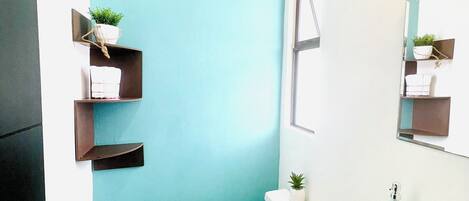 A bathroom with a blue accent wall, a toilet, a sink, and two shelves with plants.