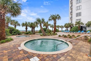 A pool area with palm trees, lounge chairs, and a building in the background.