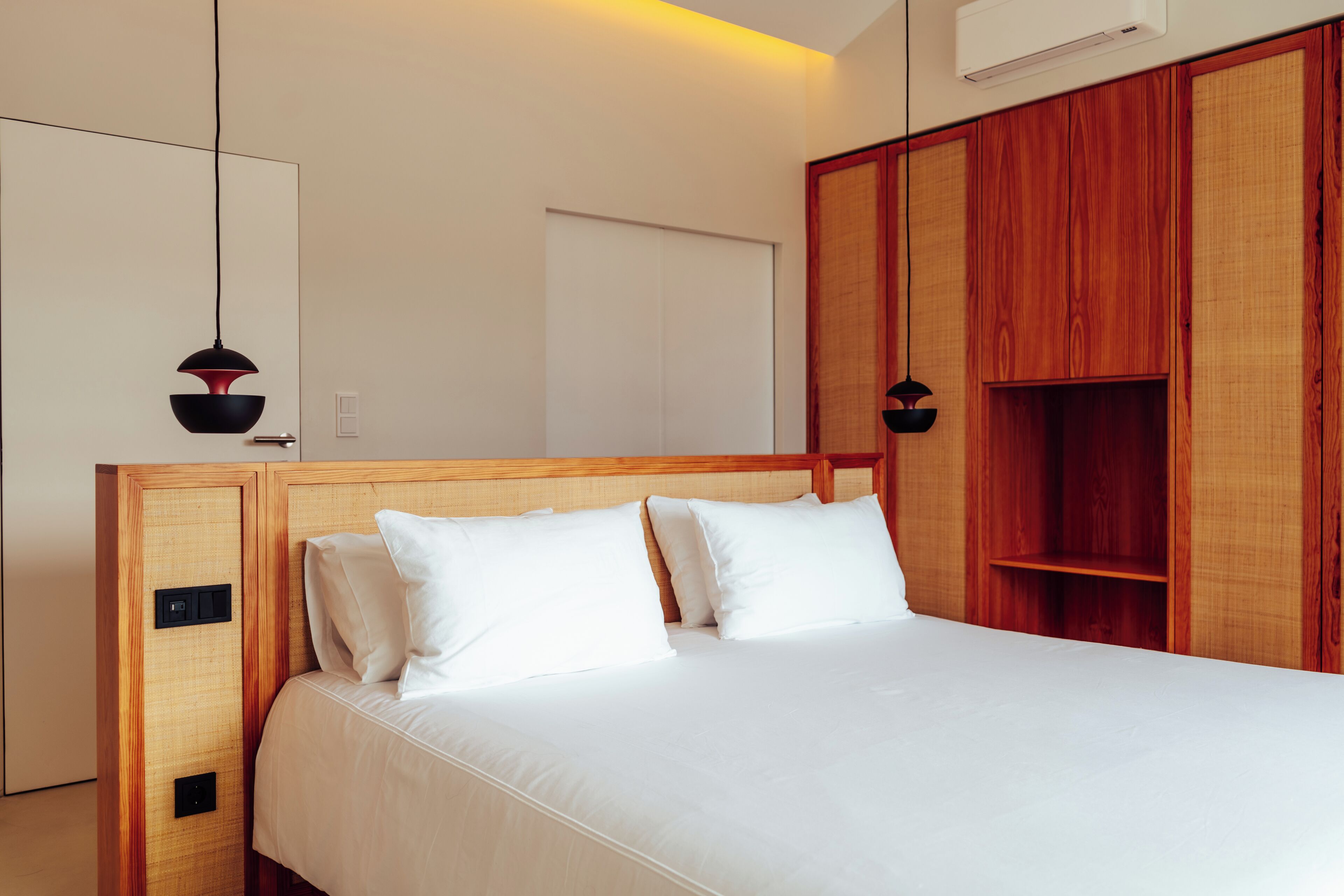 A modern bedroom with a wooden headboard, a bed with white linens, and a built-in wooden wardrobe.