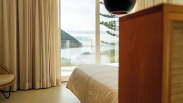 A bedroom with a large window, a bed, a chair, and a wooden cabinet.