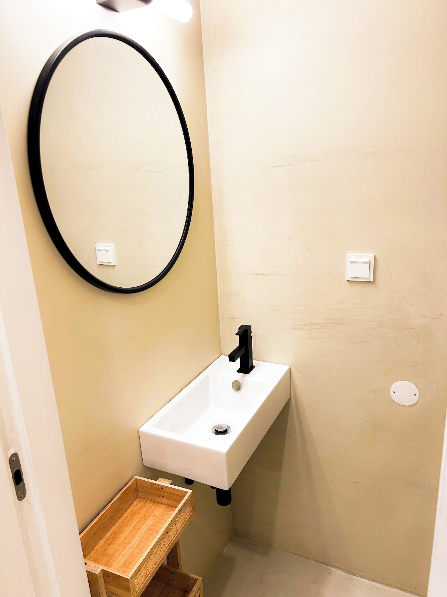 Une petite salle de bain avec un lavabo blanc, un robinet noir et une étagère en bois.