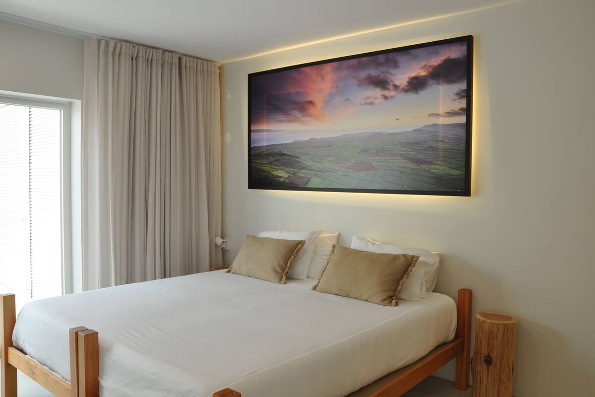 Een slaapkamer met een groot bed, uitzicht op een zonsondergang en een houten nachtkastje.