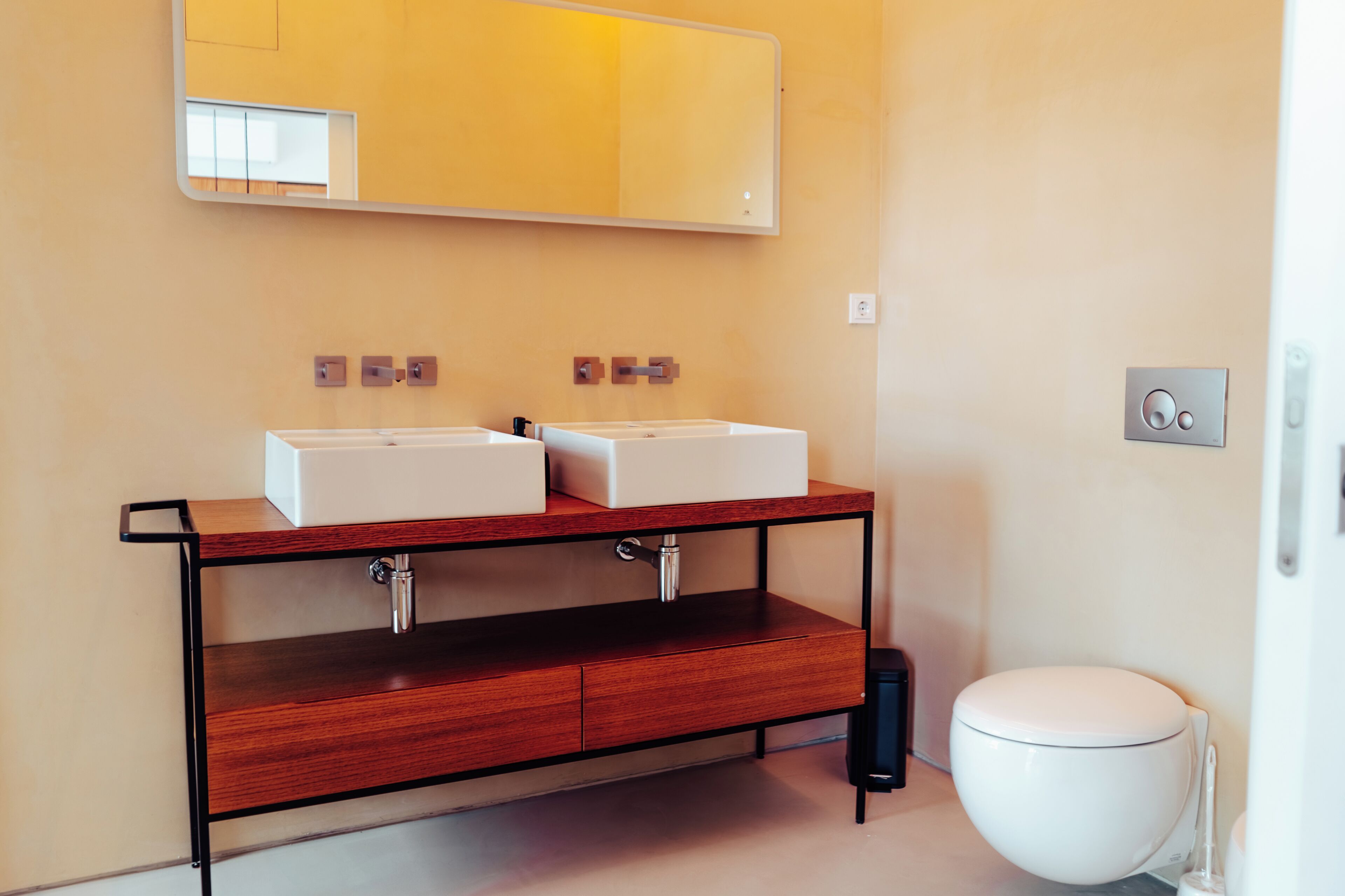 Un baño con tocador de madera, dos lavamanos, un espejo y un inodoro.