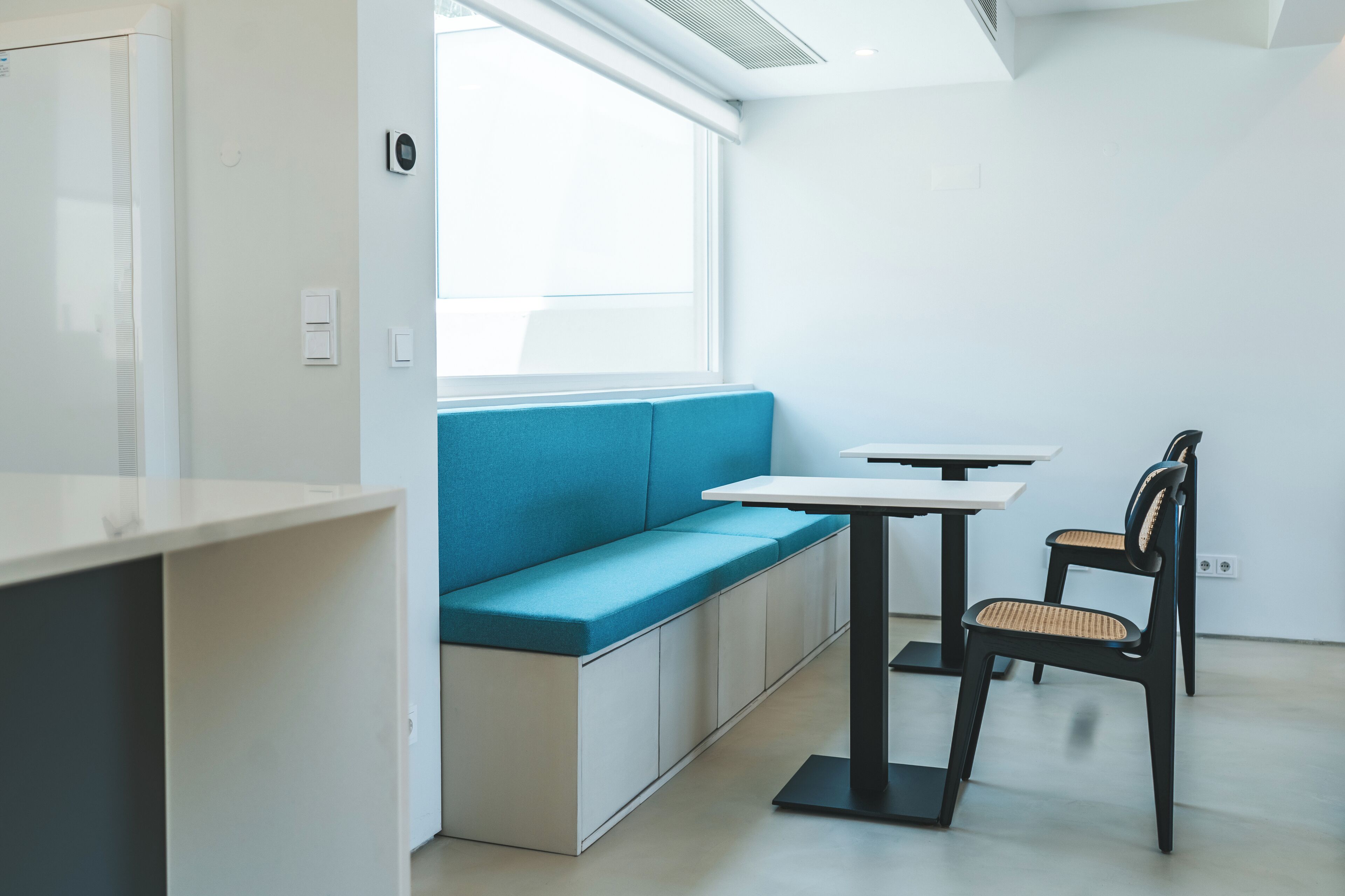A modern, minimalist room with a blue cushioned bench, a white table, and two black chairs.
