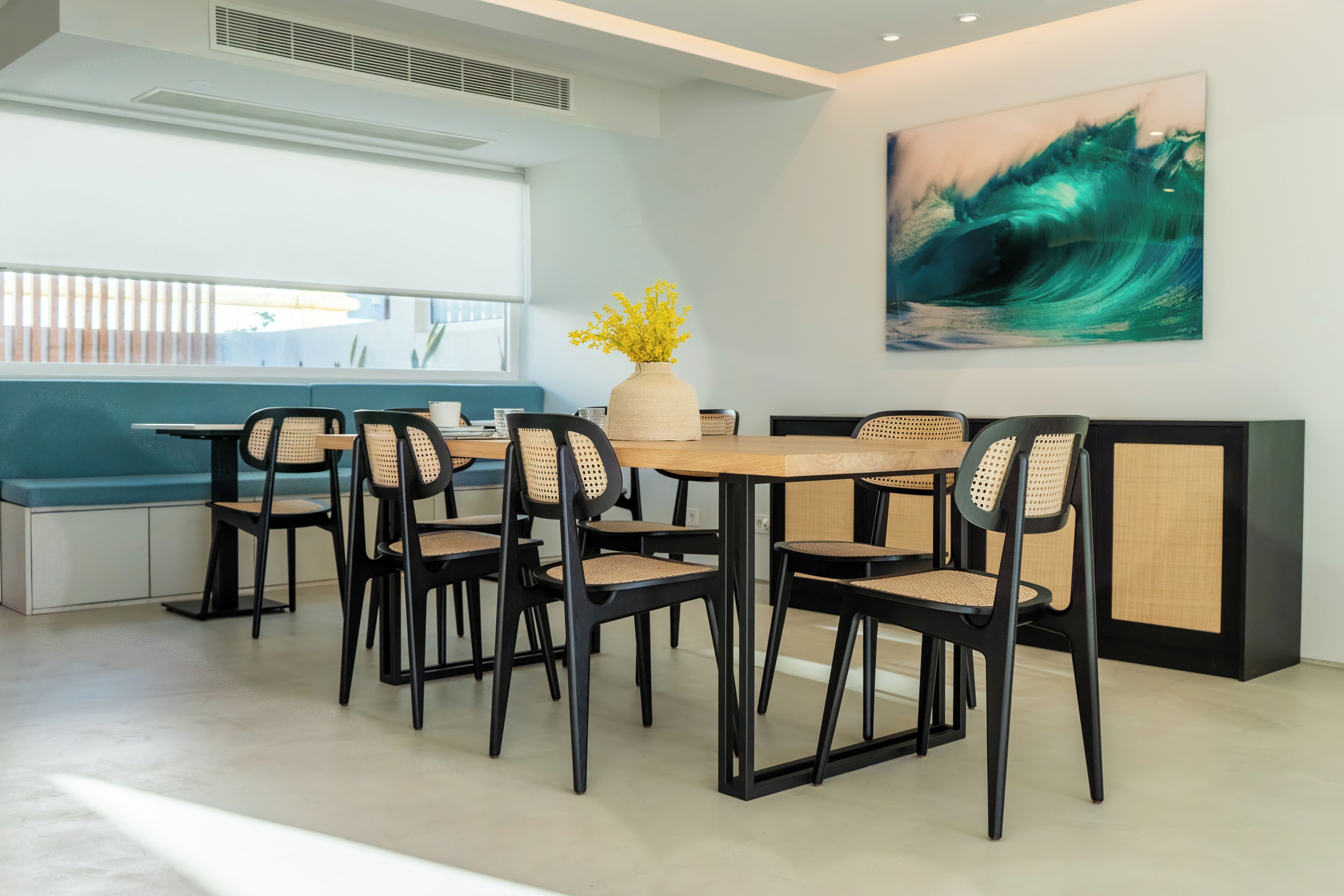 Un comedor moderno con una mesa de madera y sillas negras, un jarrón con flores amarillas y un cuadro abstracto grande en la pared.