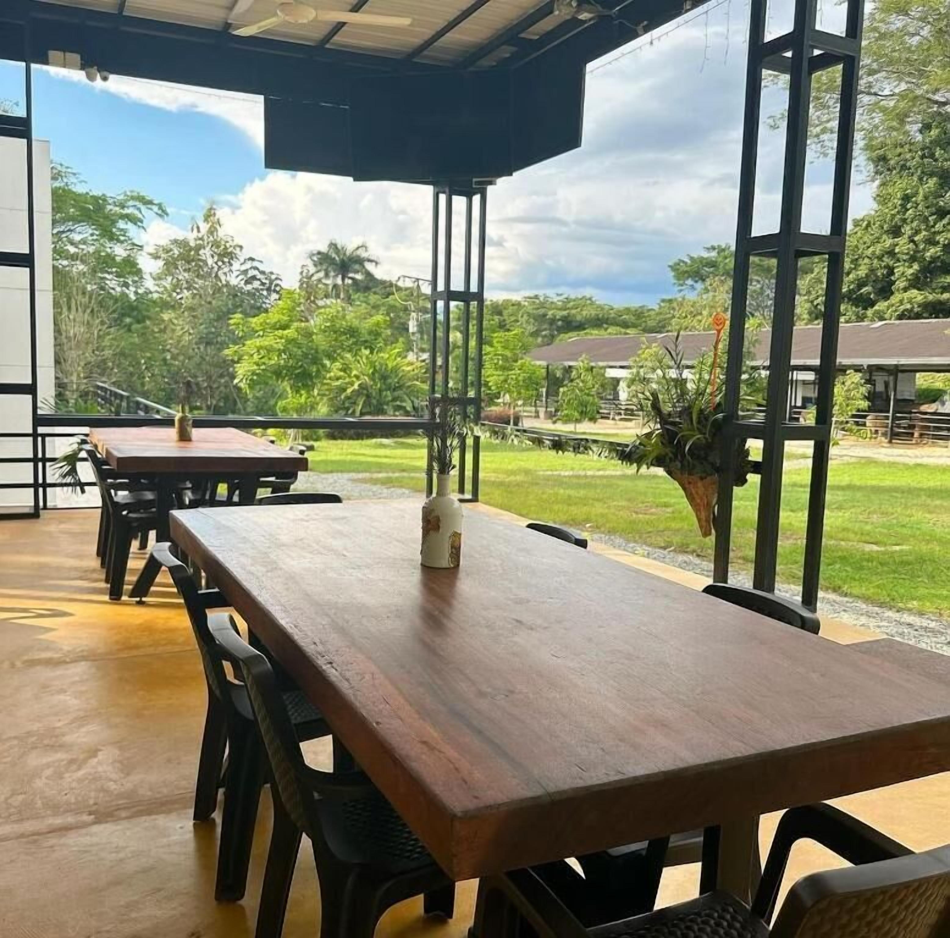 Un espacio de estar al aire libre cubierto con mesas y sillas de madera, con vistas a un paisaje con césped y árboles.