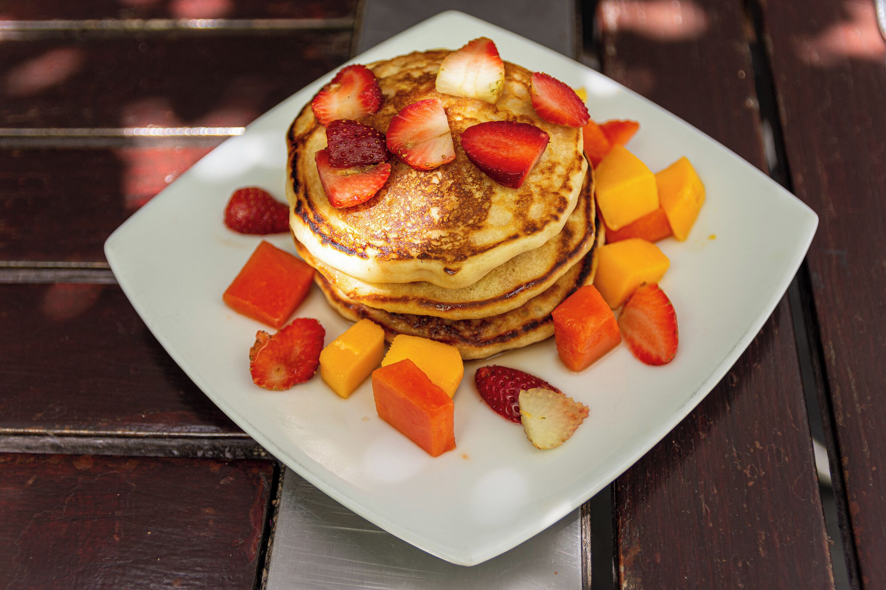 A stack of pancakes with strawberries and mango chunks on a white plate.