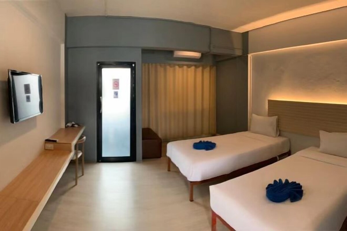 A hotel room with two beds, a desk, a TV, and a door leading to the outside.