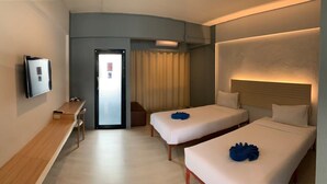 Une chambre d’hôtel avec deux lits, un bureau, une télévision et une porte dotée d’un panneau en verre dépoli.