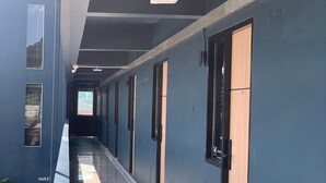 Un long couloir, avec des portes d’un seul côté, un sol carrelé et un éclairage au plafond.