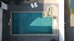 Vue aérienne d’une piscine rectangulaire dont les bords sont recouverts de carreaux, entourée d’une allée pavée.