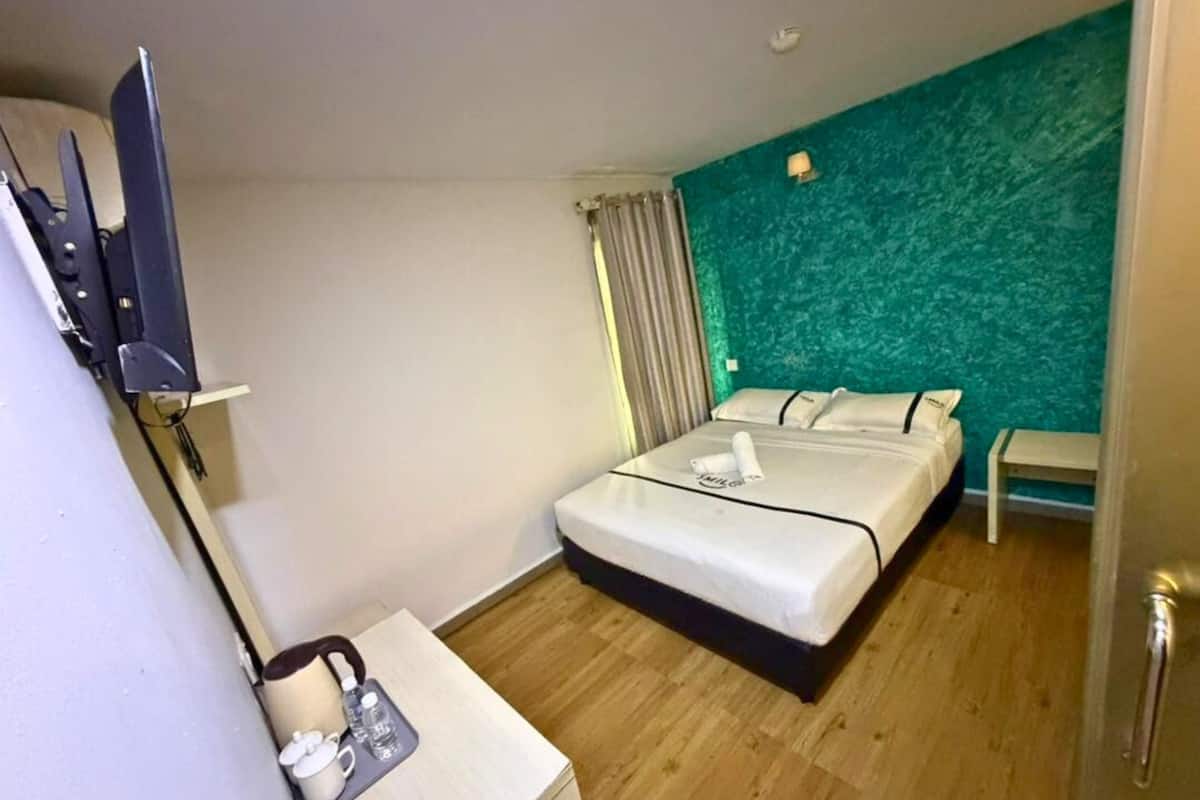 Une chambre d’hôtel avec un lit, une table de chevet avec une lampe, une télévision et une fenêtre avec des rideaux.