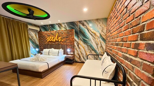 A hotel room with a brick wall, a mural, a bed with white bedding, a bedside table, and a desk. - Seeds Hotel Cheras Maluri (Kuala Lumpur)
