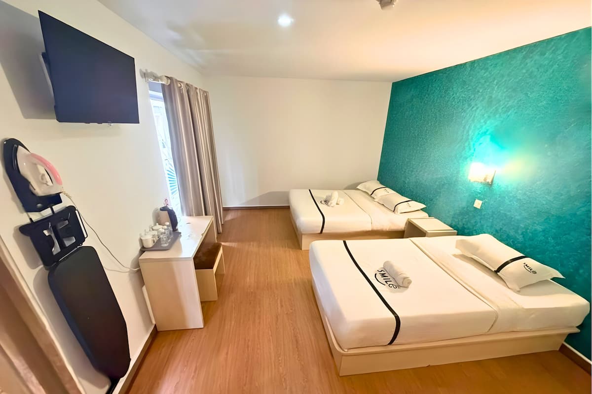 Une chambre d’hôtel avec deux lits, un bureau, un téléviseur à écran plat et un mur d’accent de couleur turquoise.