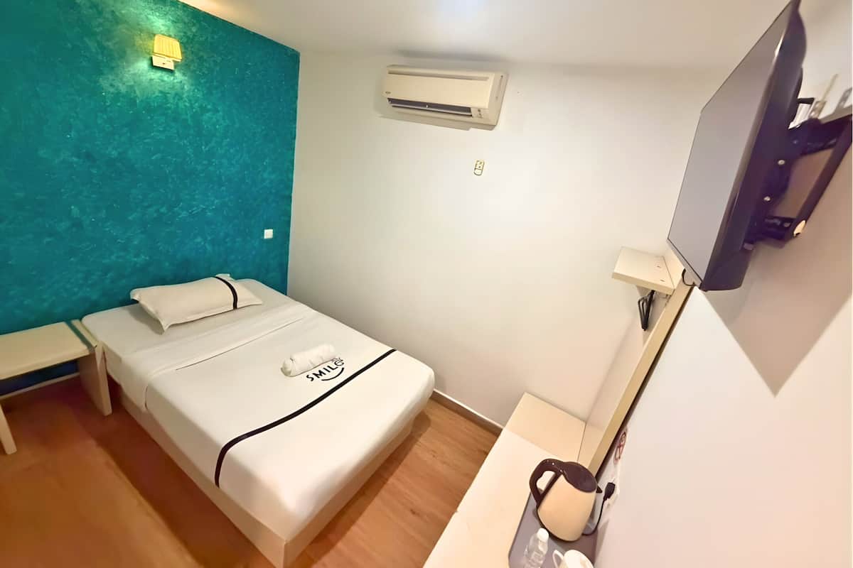 Une chambre d’hôtel équipée d’un lit, d’une table de chevet avec une lampe, d’une télévision et d’un appareil de climatisation.
