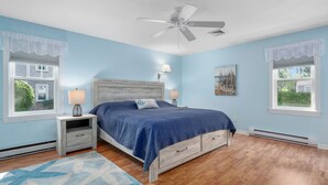 Une chambre à coucher comprenant un lit, des tables de chevet, un ventilateur de plafond et une fenêtre donnant sur un paysage verdoyant.