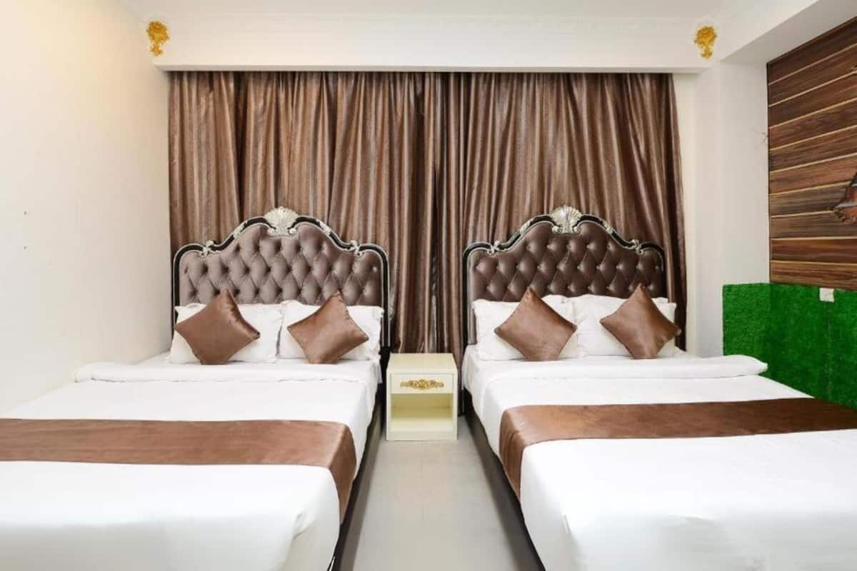A hotel room with two beds, each with a tufted headboard, white bedding, and brown throw blankets.