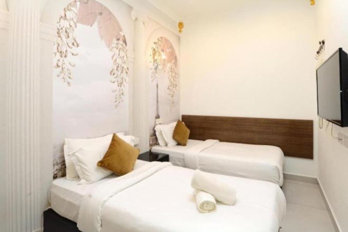 Une chambre d’hôtel avec deux lits, du linge de lit blanc, une tête de lit en bois et un téléviseur à écran plat.