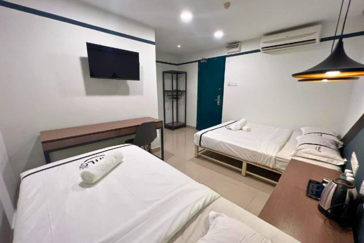 A hotel room with two single beds, a desk, a chair, a TV mounted on the wall, and an air conditioning unit.