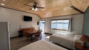Een kamer met twee bedden, een houten plafond, een eettafel met stoelen, een televisie aan de muur en een raam met uitzicht op het water.