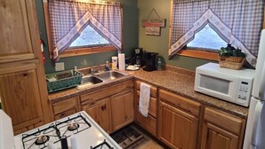 Una cocina con armarios de madera, estufa a gas, lavamanos, microondas y ventana con cortinas escocesas.