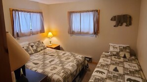 Un dormitorio con dos camas, una mesita de noche, una lámpara y una decoración de oso en la pared.