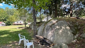 A large rock formation with a log and two white plastic chairs in a grassy area. - 4th Lake Front Cliff Camp @ Eagle Bay Village (Eagle Bay)