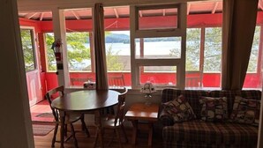 A cozy room with a wooden table and chairs, a plaid sofa, and large windows offering a view of the outdoors. - 4th Lake Front Cliff Camp @ Eagle Bay Village (Eagle Bay)