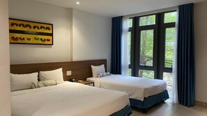Een hotelkamer met twee bedden, een groot raam met gordijnen en een schilderij aan de muur.