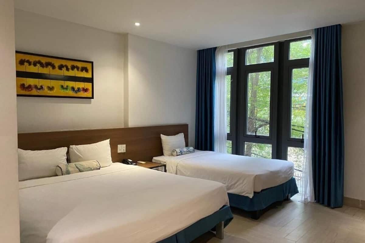 A hotel room with two beds, a large window with curtains, and a painting on the wall.