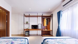 Een hotelkamer met twee bedden, een bureau met een computer, een kledingkast en een raam met gordijnen.