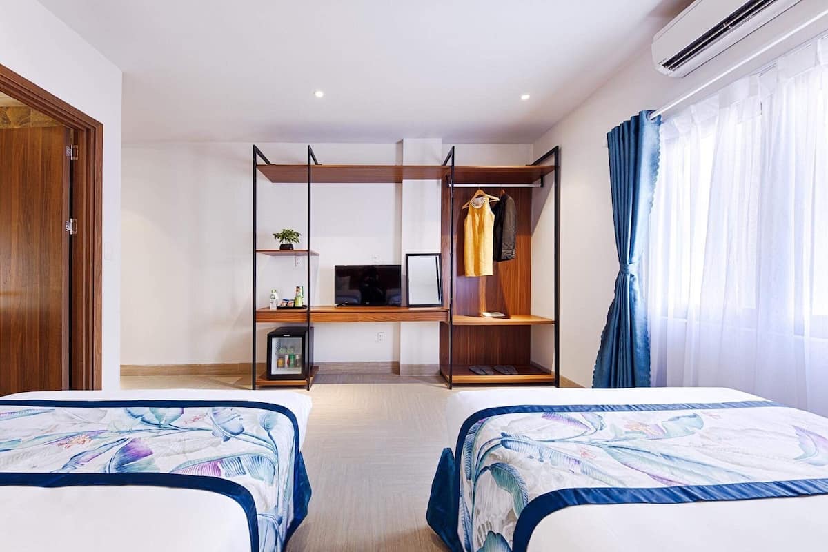 A hotel room with two beds, a desk with a computer, a wardrobe, and a window with curtains.