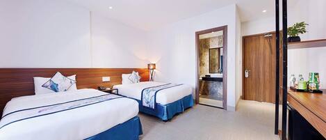 Une chambre d’hôtel avec deux lits, une tête de lit en bois, une table de chevet, une lampe, un miroir, une porte et une petite étagère avec des bouteilles.