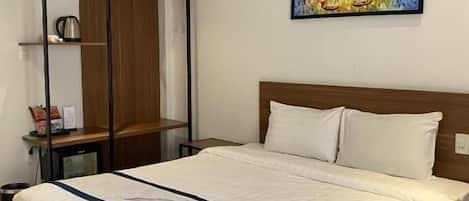 A hotel room with a large bed, a wooden wardrobe, a painting on the wall, and a small table with a kettle.