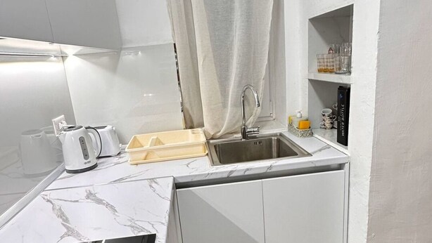 A compact kitchen with white cabinets, a sink, a stove, and a small countertop.