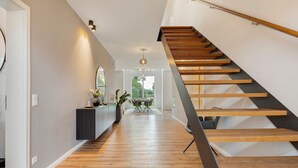 A modern interior with a wooden staircase, a hallway leading to a dining area, and a view of greenery outside. - Holiday Home 'Luxurious Family House' with Terrace and Wi-Fi (Tornesch)
