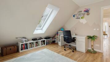Una habitación con techo inclinado, escritorio, silla, estantería, un globo terráqueo y una planta.