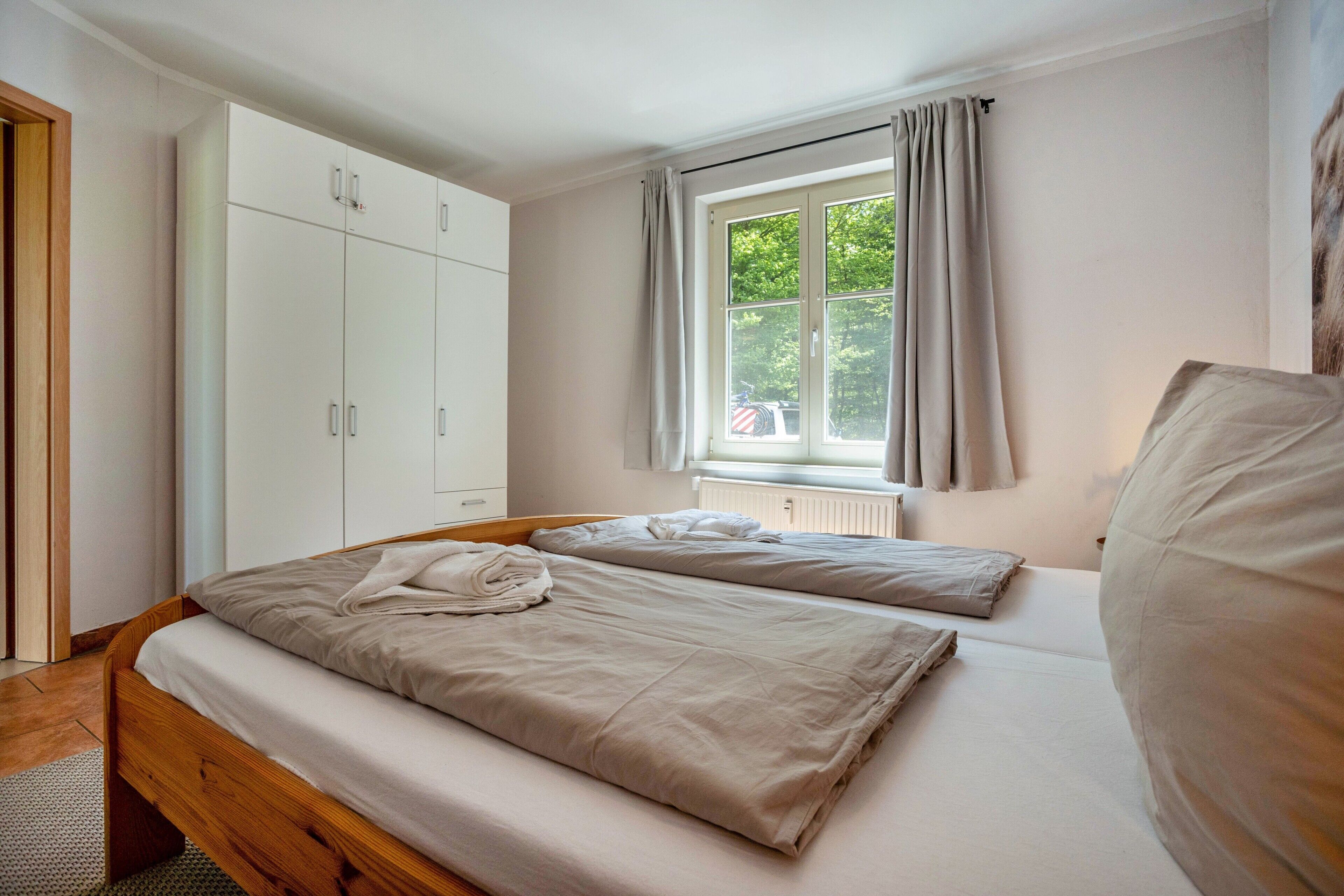 A bedroom with a bed, a wardrobe, a window with curtains, and a radiator.