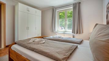A bedroom with a bed, a wardrobe, a window with curtains, and a radiator.
